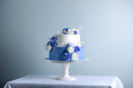 Beautiful two tiered white and blue wedding cake decorated with flowers sugar roses on the table....
