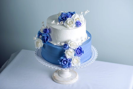 Beautiful two tiered white and blue wedding cake decorated with flowers sugar roses on the table....