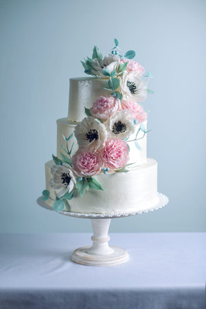 Beautiful three tiered white wedding cake decorated with flowers sugar pink peonies and green leaves...
