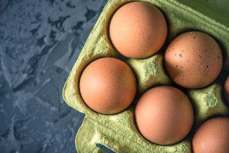 Brown fresh farm eggs in green tray, on beautiful dark background. Home eco-friendly products