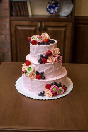 Beautiful elegant three tiered pink wedding cake decorated with berries and flowers. The concept patisserie floristic from sugar masticの写真素材