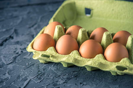 Brown fresh farm eggs in green tray, on beautiful dark background. Home eco-friendly productsの写真素材