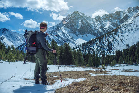 Man Hiker with trekking poles stands in the snowy mountains at the foot of the peak in Sunny weather. The concept of travel and achieve the goalの写真素材