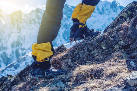 Climber in crampons stands on the rocks in front of the entrance to the peak on the background of the snowy mountains. Feet close up. The concept of the travel path and achieving the goalの写真素材