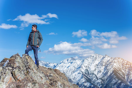 Man Hiker stands on top and looks up at the sky and snowy mountains around in Sunny weather. The...