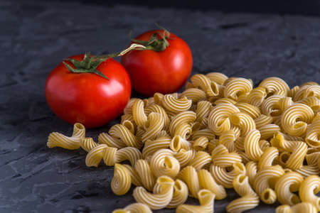 Uncooked italian pasta cavatappi with ingredients for tomato sauce on a dark background. The concept of the composition of food design.の写真素材