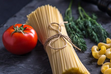 Uncooked italian pasta cavatappi and spaghetti with ingredients for tomato sauce on a dark...