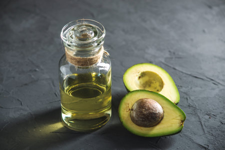 Green avocado fruit and oil in glass bottle on dark background. Concept organic eco products for...
