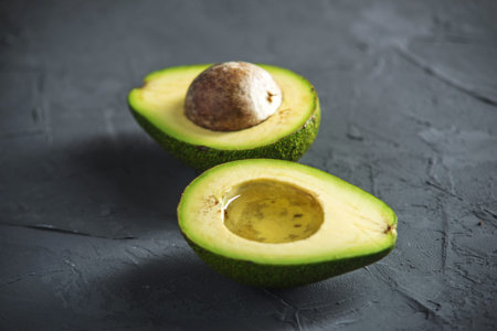 The oil flowing from the avocado fruit cut in half on the dark background. Concept organic eco...