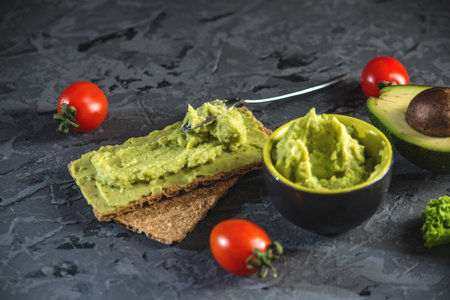 Traditional Mexican cold appetizer made of pureed avocado pulp with bread and vegetables on a dark...