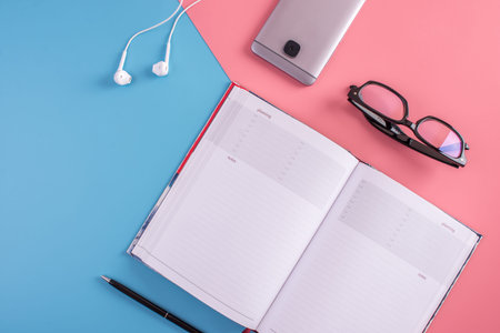 Laptop, glasses, pen, notebook and phone with headphones on pastel background. The view from the...