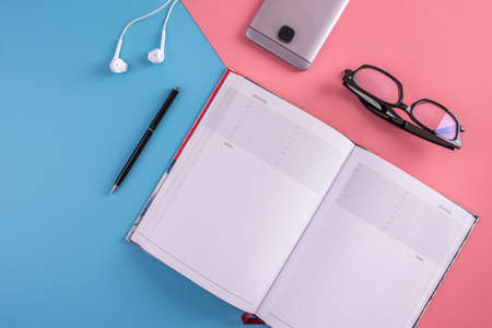 Laptop, glasses, pen, notebook and phone with headphones on pastel background. The view from the top. The concept of planningの写真素材