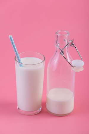Glass bottle of fresh milk and a glass with a straw on a pink background.の写真素材