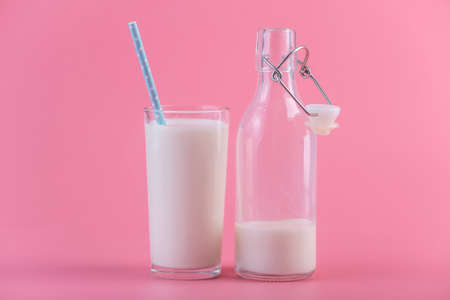 Glass bottle of fresh milk and a glass with a straw on a pink background.の写真素材