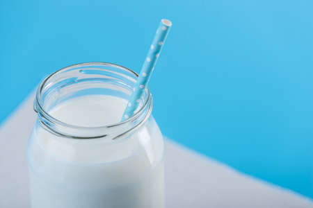 Glass bottle of fresh milk with straw on blue background.の写真素材