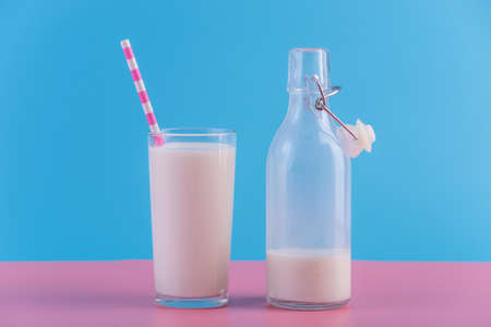 Glass bottle of fresh milk and a glass with a straw on a pastel background.の写真素材