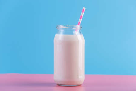 Glass bottle of fresh milk with straw on pastel background.の写真素材