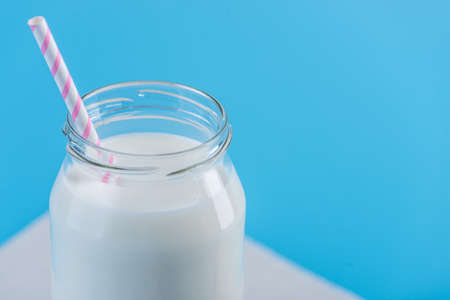 Glass bottle of fresh milk with straw on blue background.の写真素材