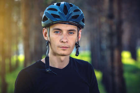 Man cyclist is wearing a sports gray helmet on his head in the background of green nature. The concept of mandatory protection during Cyclingの写真素材