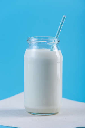 Glass bottle of fresh milk with straw on blue background. Colorful minimalism. The concept of healthy dairy products with calciumの写真素材