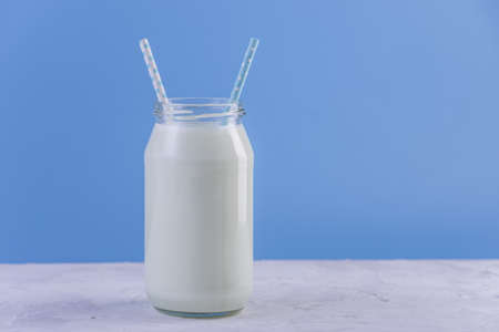 Glass bottle of fresh milk with two straws on blue background. Colorful minimalism. The concept of healthy dairy products with calciumの写真素材