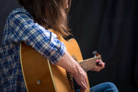The girl teenager playing an acoustic guitar on a dark background in the Studio. Concert young musiciansの写真素材
