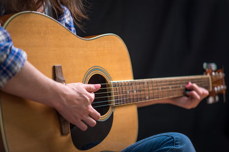 The girl playing an acoustic guitar on a dark background in the Studio. Concert young musicians