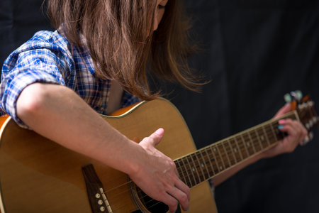 The girl teenager playing an acoustic guitar on a dark background in the Studio. Concert young musiciansの写真素材