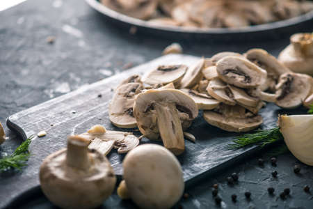 White fresh sliced champignons in a pan on the dark kitchen table. The concept of cooking mushroom dishes. Close upの写真素材