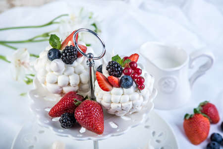Delicate white meringues with fresh berries on the plate. Dessert Pavlova. White background. A festive wedding cake.の写真素材