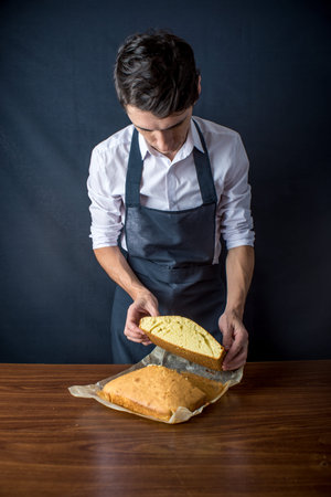 Young man chef in uniform black apron is holding a freshly baked biscuit. The concept of men cook...