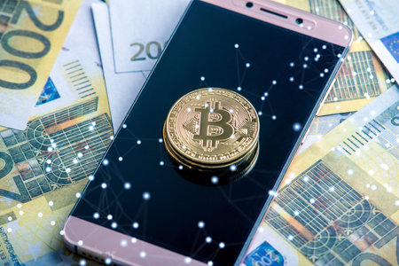 Physical bitcoin coin on the phone screen on the background of Euro banknotes. The concept of...