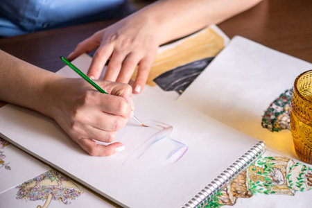 Women's beautiful hands paint with a brush watercolor sketch of the cake on a white sheet of paper.