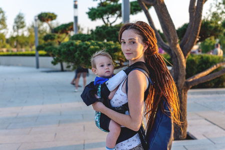 Young happy mom with baby son in ergo backpack travel together. Sunny summer day. The concept of...