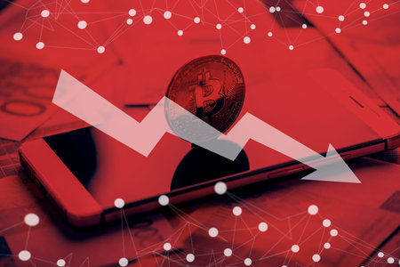 Physical bitcoin coin on the phone screen on the background of the Euro banknotes. Red arrow of the chart of falling quotes downの写真素材