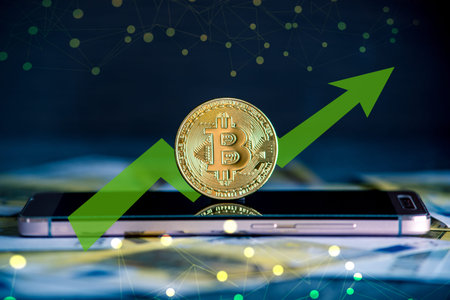 Physical bitcoin coin on the phone screen on the background of the Euro banknotes. Green arrow of the price growth chartの写真素材