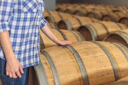 Woman winemaker checks oak wine barrels in which red wine is aged in the basement of the winery. The...