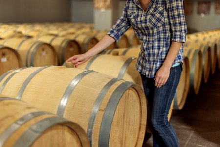 Woman winemaker checks oak wine barrels in which red wine is aged in the basement of the winery. The...