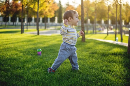 Cute baby runs on a green lawn runing in nature on a Sunny autumn day. One-year-old child. The...