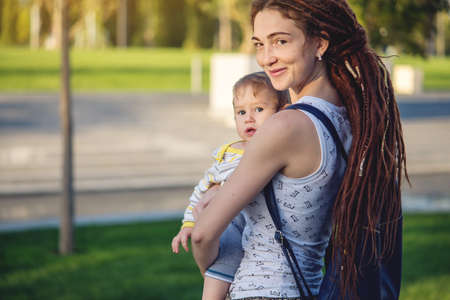 Young modern happy mom with baby son walking in Sunny Park. The concept of the joy of motherhood and autumn moodの写真素材