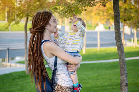 Young modern happy mom with baby son walking in Sunny Park. The concept of the joy of motherhood and autumn moodの写真素材