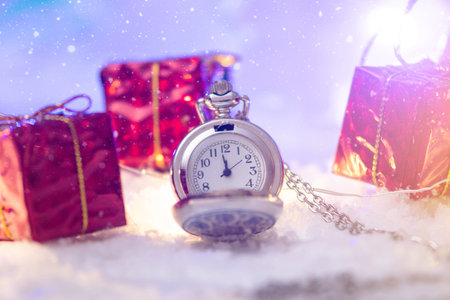 Pocket watch with a dial in the snow with gifts on the eve of holidays. Concept waiting for the...
