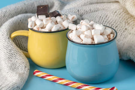 Mugs of hot chocolate with marshmallows on top and stick a Lollipop on a blue background. Concept of a cozy warm Christmas home holidayの写真素材
