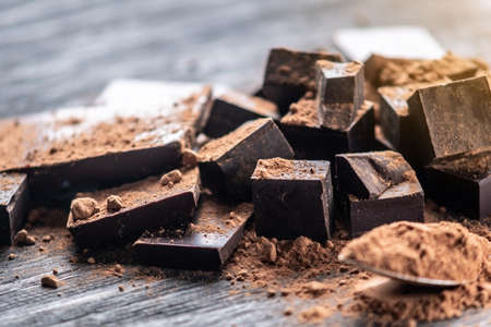 Pieces of dark bitter chocolate with cocoa powder on dark wooden background. The concept of confectionery ingredientsの写真素材