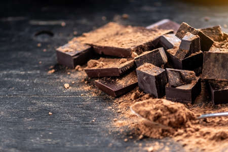 Pieces of dark bitter chocolate with cocoa powder on dark wooden background. The concept of confectionery ingredientsの写真素材