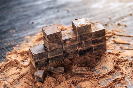 Pieces of dark bitter chocolate with cocoa powder on dark wooden background. The concept of confectionery ingredientsの写真素材