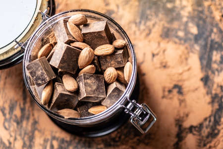 Pieces of dark bitter chocolate with cocoa powder and nuts almonds on wooden background. The concept of confectionery ingredientsの写真素材