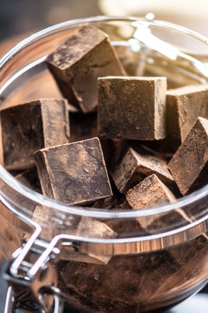 Pieces of dark bitter chocolate with cocoa powder in a glass jar on wooden background. The concept...