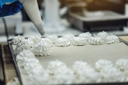 The process of making meringue and desserts. A gloved hand squeezes the cream. Production of confectioneryの写真素材