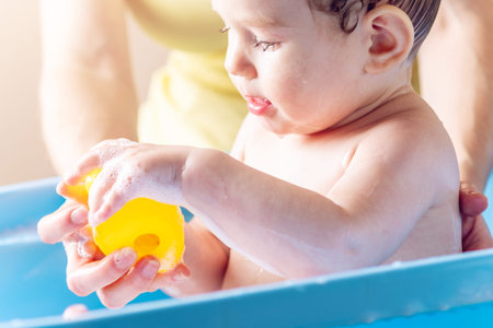 Mom washing little boy in a blue bath. The child is bathing with a yellow duck. Hygiene and water...